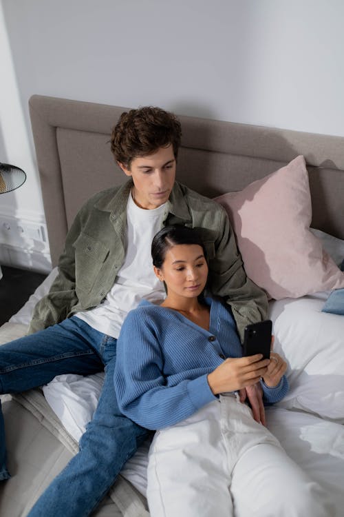 Couple Lying on Bed Looking at the Smartphone 