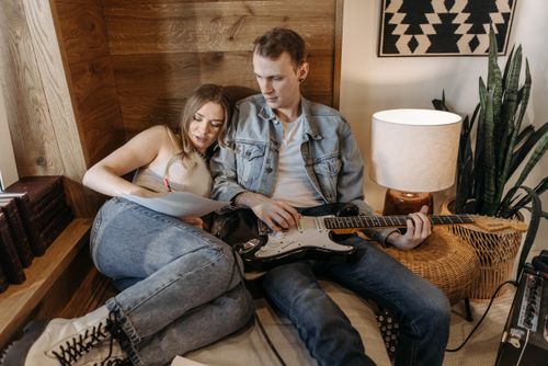 Free A man playing electric guitar while a woman writes in a cozy room setting. Stock Photo