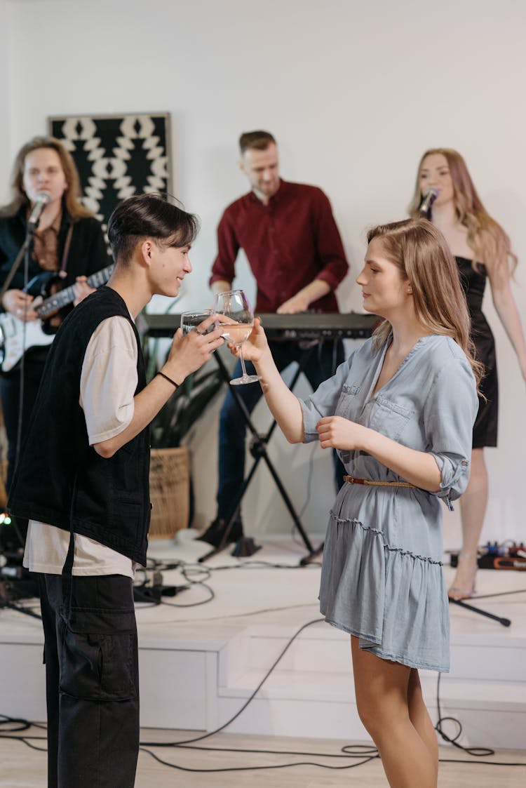 A Man And Woman Toasting Drinks While Standing In Front Of The Band Playing Music