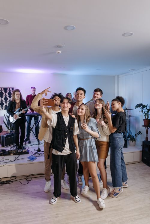 Free A group of diverse young adults enjoying an indoor concert, capturing fun moments with a selfie. Stock Photo