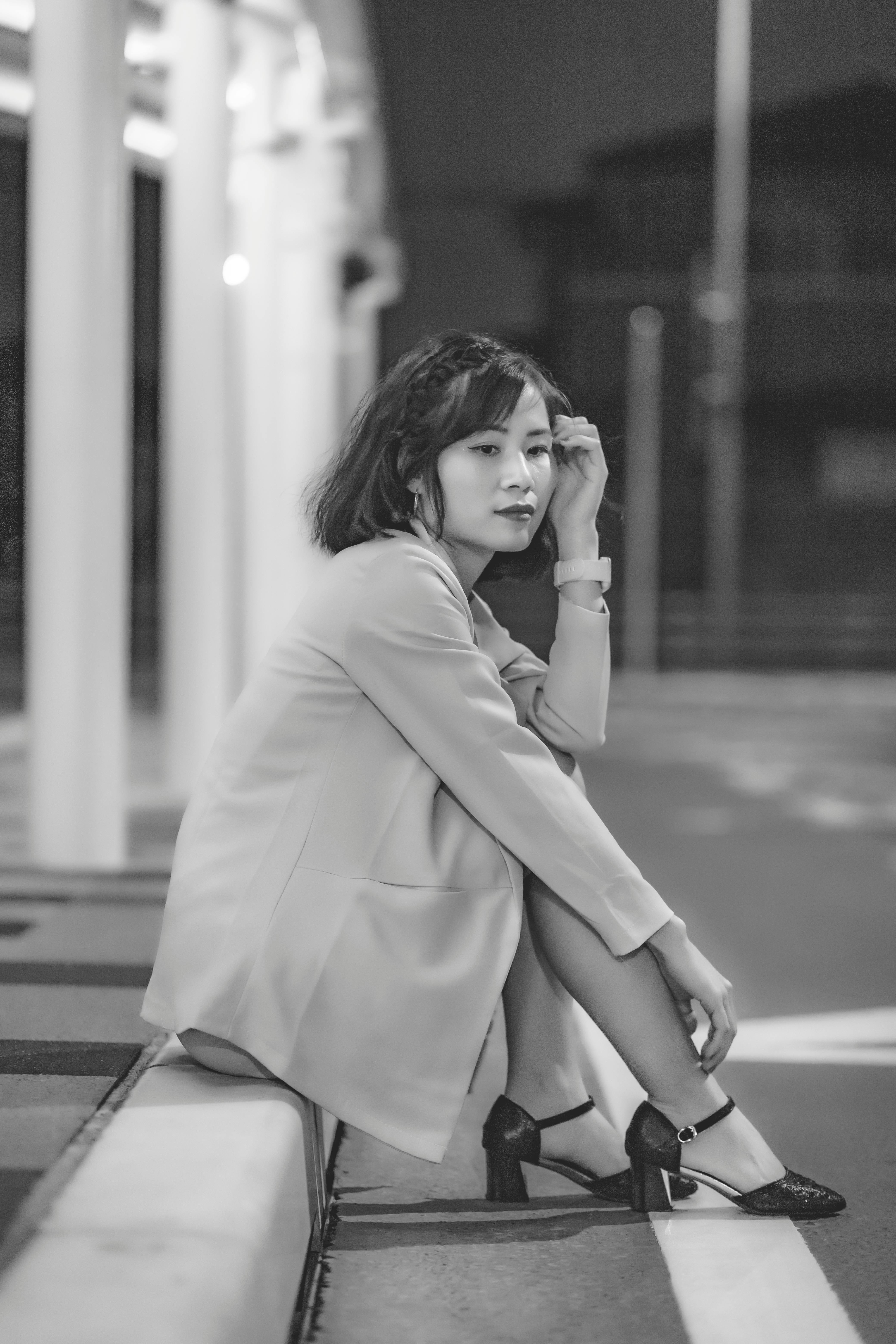 Black and white image of a woman sitting on a sidewalk, exuding elegance and contemplation.