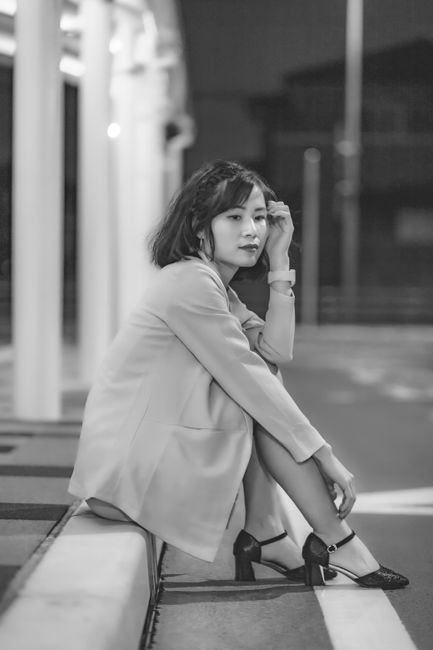 Black and white image of a woman sitting on a sidewalk, exuding elegance and contemplation.