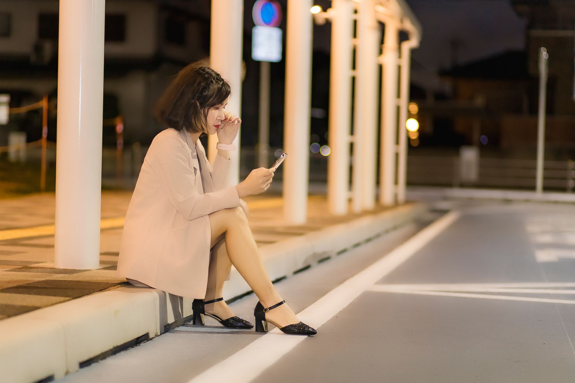 Jeune femme assise sur un trottoir la nuit, regardant l'écran de son smartphone