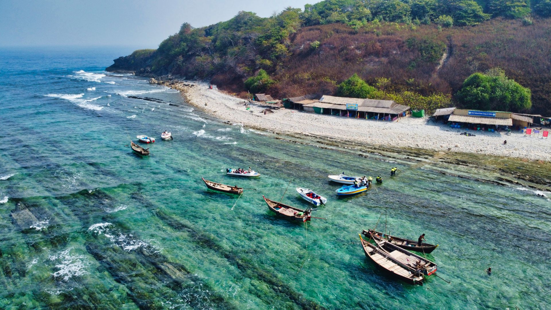 Scenic aerial view of traditional boats along the Myanmar coastline, showcasing clear waters and vibrant shore.