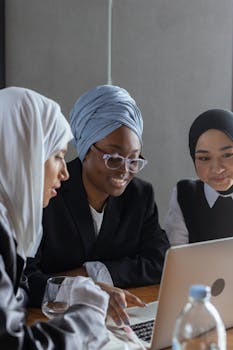 A group of diverse businesswomen in hijabs working together on a laptop in an office.