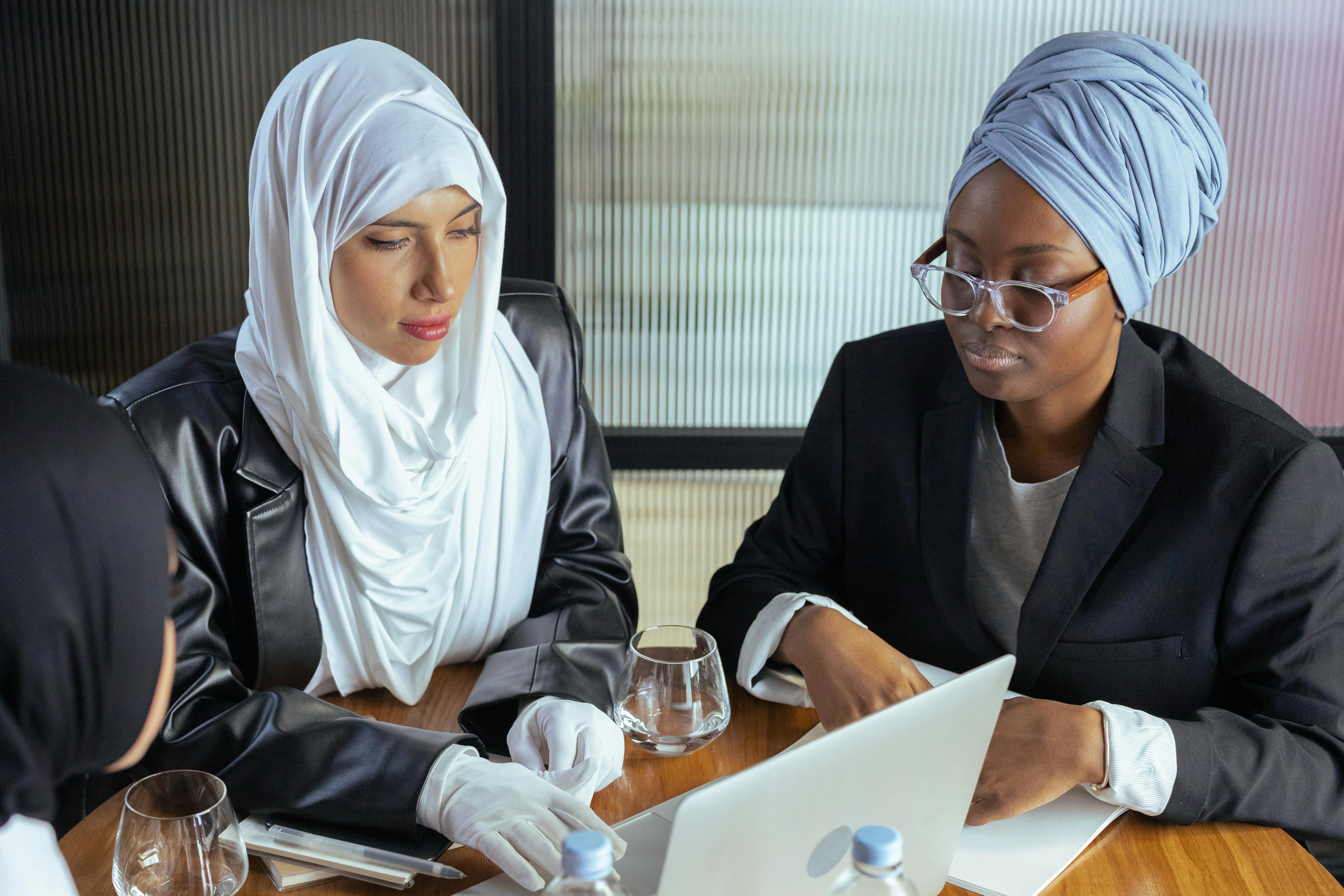 woman in white hijab sitting beside a woman in black blazer