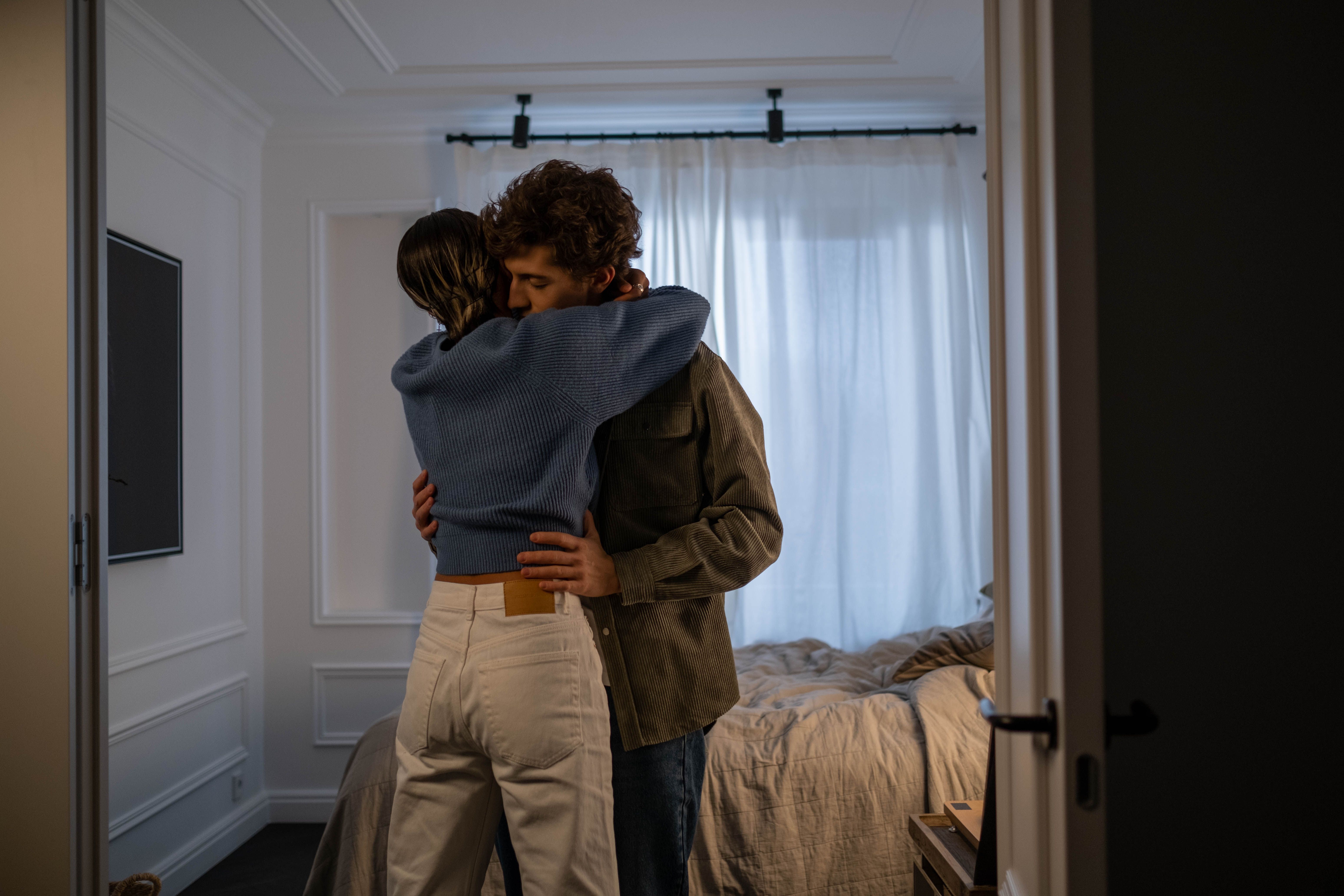 A heartfelt embrace between a loving couple in a sunlit bedroom, conveying warmth and affection.