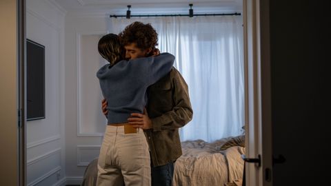 A heartfelt embrace between a loving couple in a sunlit bedroom, conveying warmth and affection.