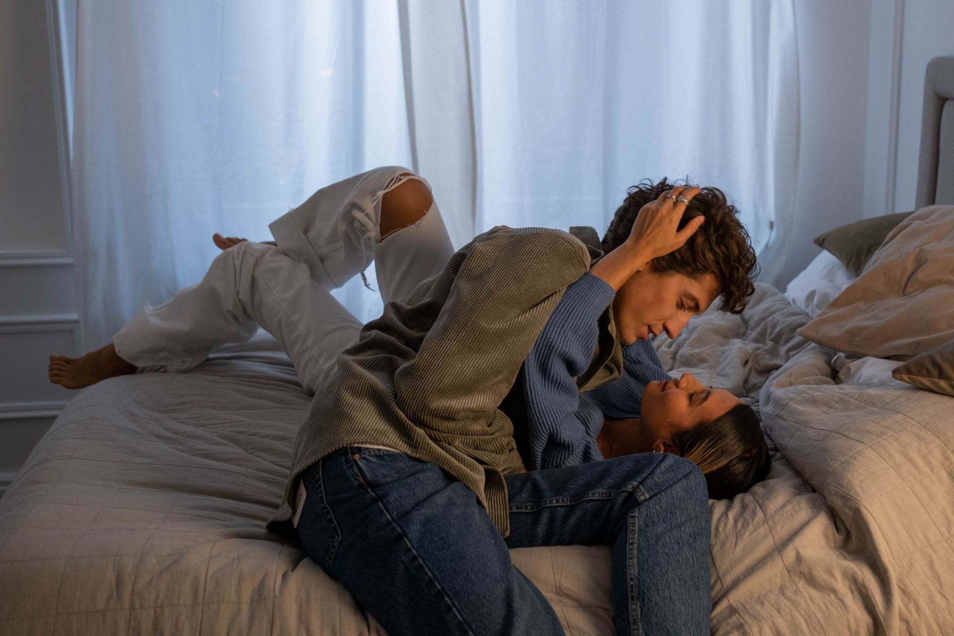 Intimate moment of a couple embracing on a bed in a softly lit bedroom environment.