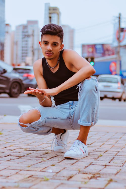 Cool young ethnic guy sitting on haunches on city street