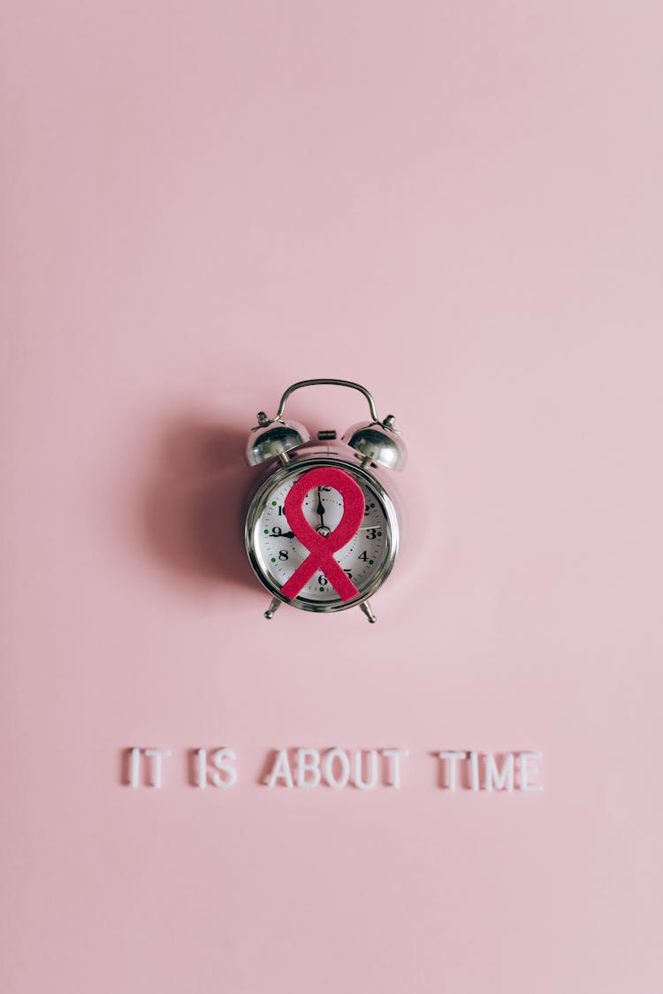 Clock With Pink Ribbon On Studio Background