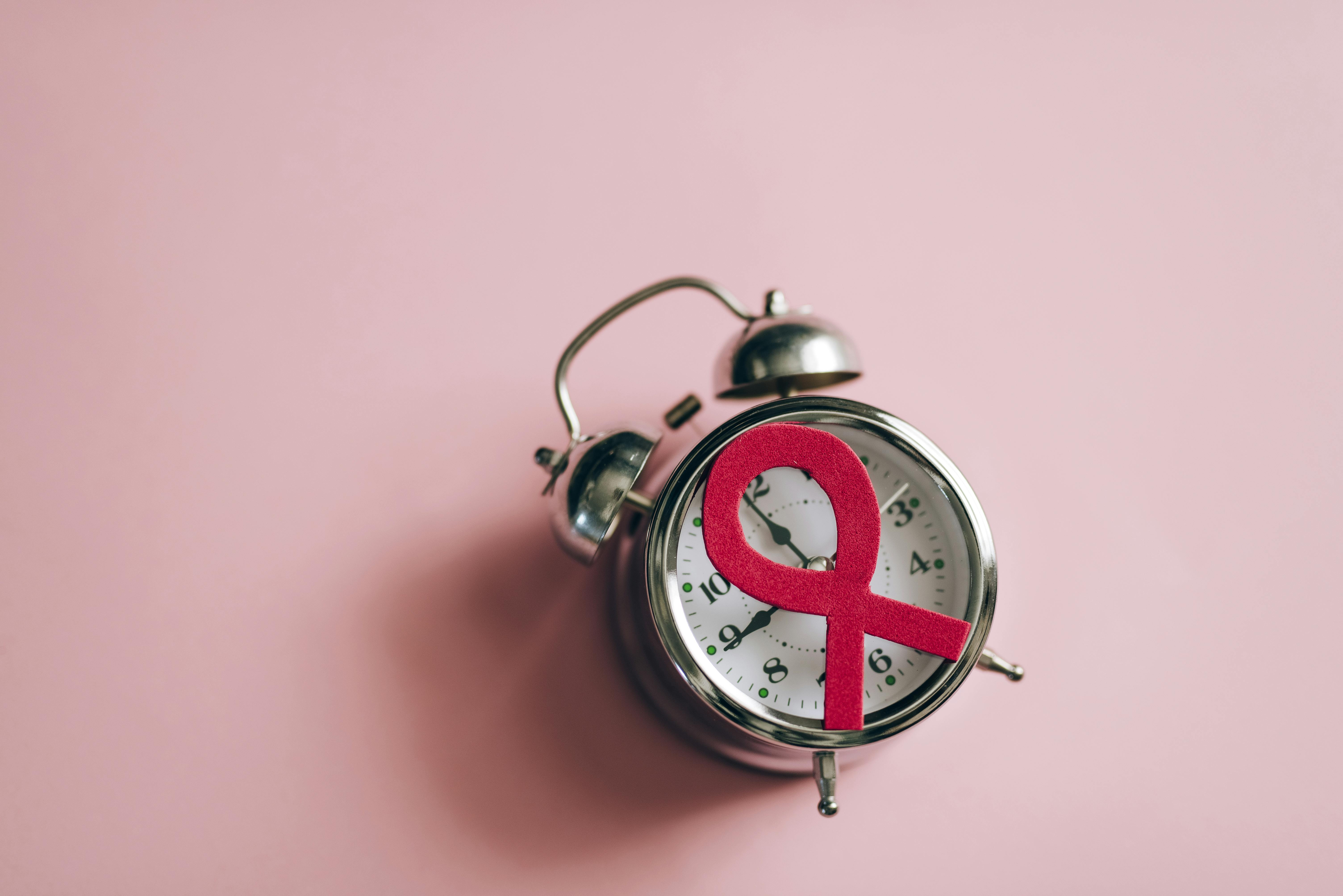 A still life of a pink ribbon on an alarm clock symbolizing breast cancer awareness.