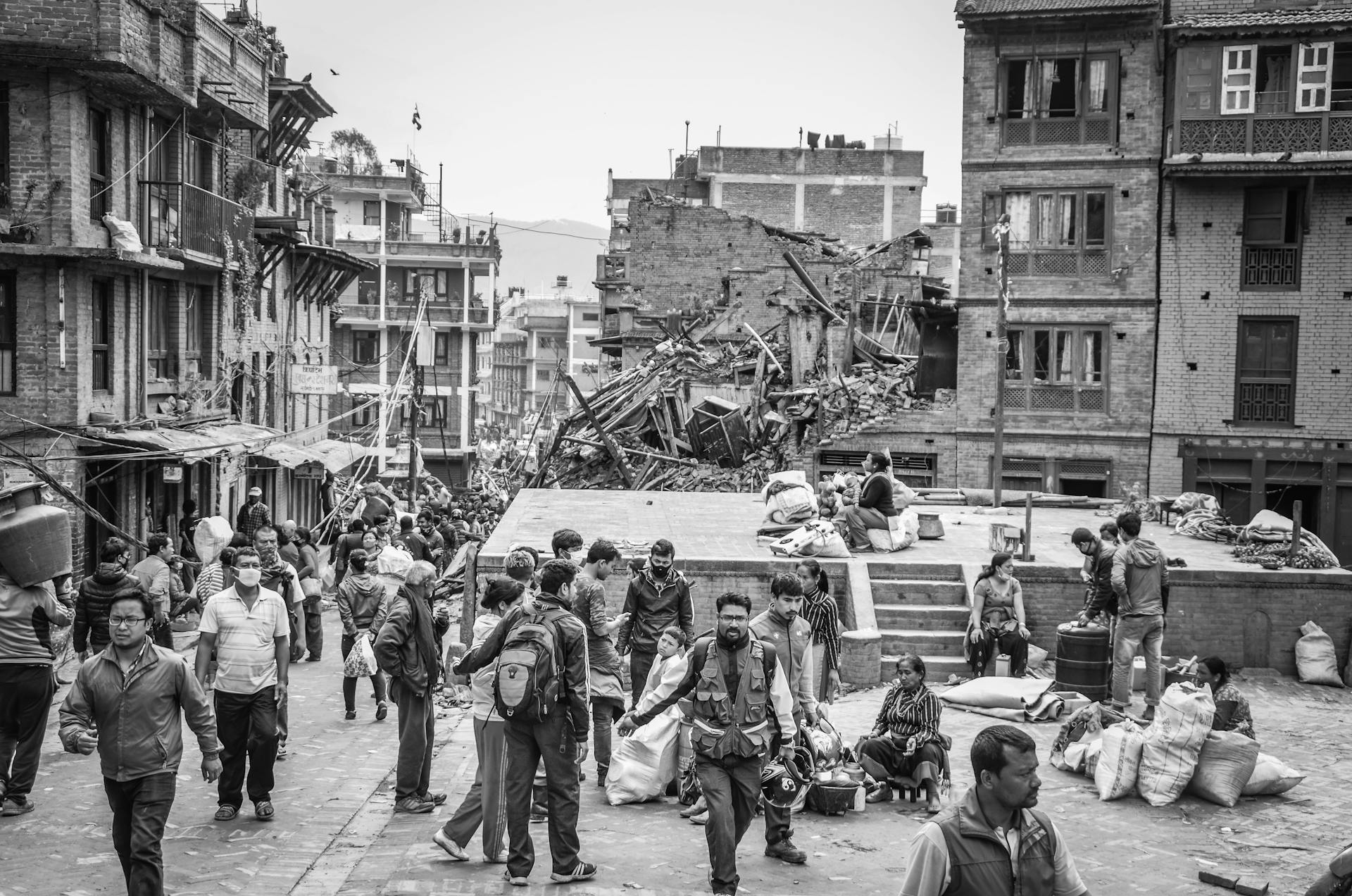 Grayscale photo showing earthquake aftermath in Bhaktapur, with people amidst debris and damaged buildings.