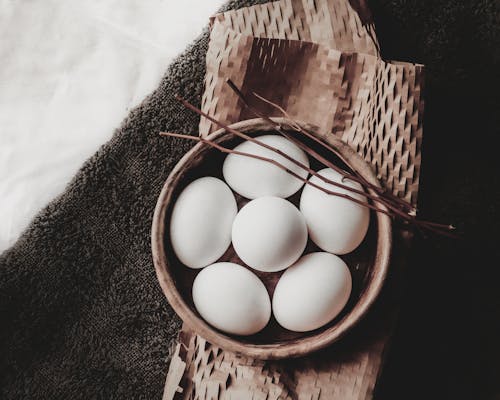 Free From above of eggs in wicker bowl with branches placed on paper above towel Stock Photo