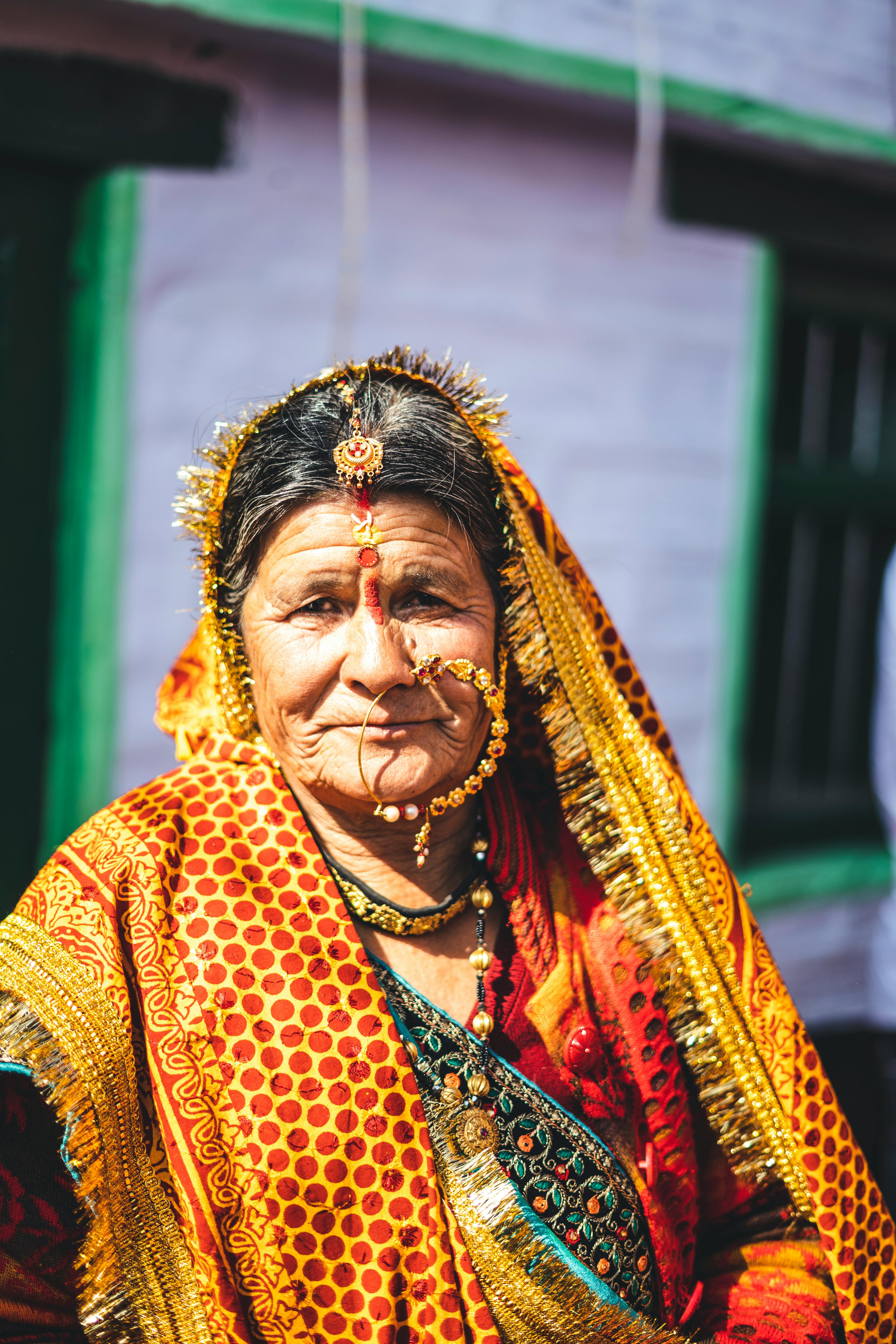 Close-up portrait of an elderly woman wearing colorful traditional Indian attire with jewelry and a headscarf.