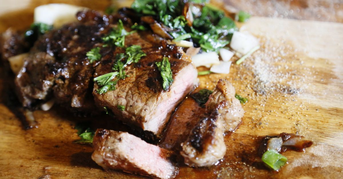 Bife grelhado chiando servido com ervas frescas em uma tábua de corte.