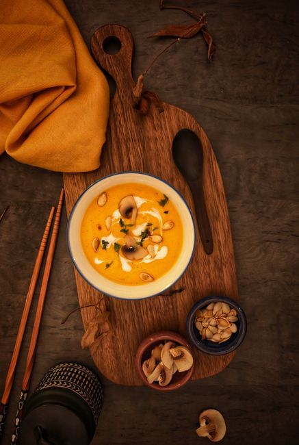 Warm, creamy pumpkin soup garnished with mushrooms, captured in an artistic overhead shot on a wooden board.