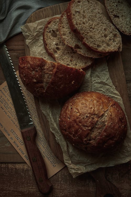 A Bread Knife beside Breads on a Wooden Chopping Board