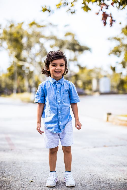 Free A cheerful child in a blue shirt and shorts, standing outdoors on a bright sunny day. Stock Photo