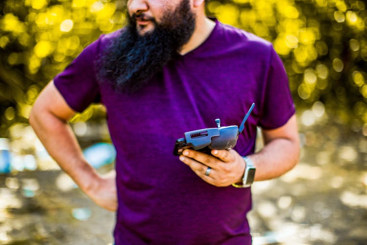 Man Standing With Smartphone With Controller For Drone In Hand In Daytime