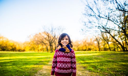 Free A happy child wearing a red sweater and scarf smiles outdoors on a sunny autumn day. Stock Photo
