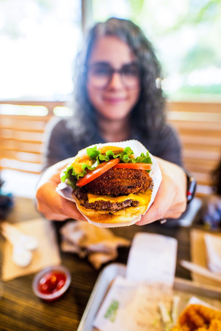 Female Showing Tasty Burger In Cafe