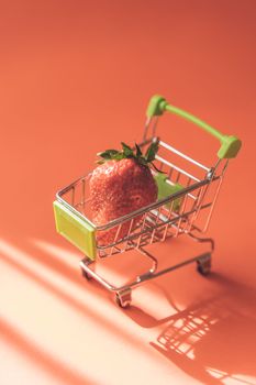 From above of small shopping trolley with strawberry representing concept of consumption and choosing food