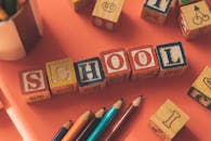 From above of wooden cubes making word school placed near color pencils on red table