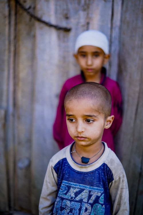 Free Two young children stand pensively against a wooden backdrop, capturing a moment of contemplation. Stock Photo