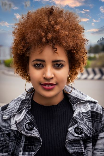 Close-up portrait of a woman with afro hair in a checkered shirt and hoop earrings against an Ethiopian backdrop.