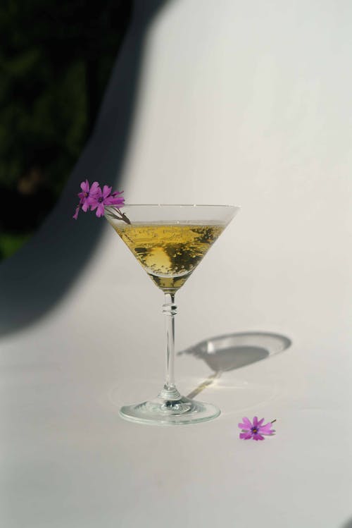 Crystal glass with alcoholic sparkling drink and delicate purple flowers placed on white background