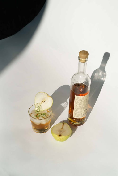 From above of glass bottle near fresh cold cocktail on white background of studio