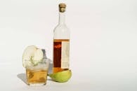 Glass bottle of calvados with halved pear and rosemary sprigs placed on white background