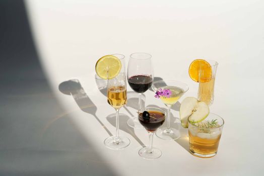 High angle of crystal glasses filled with champagne red wine Manhattan with olive on toothpick martini near pear calvados in white studio