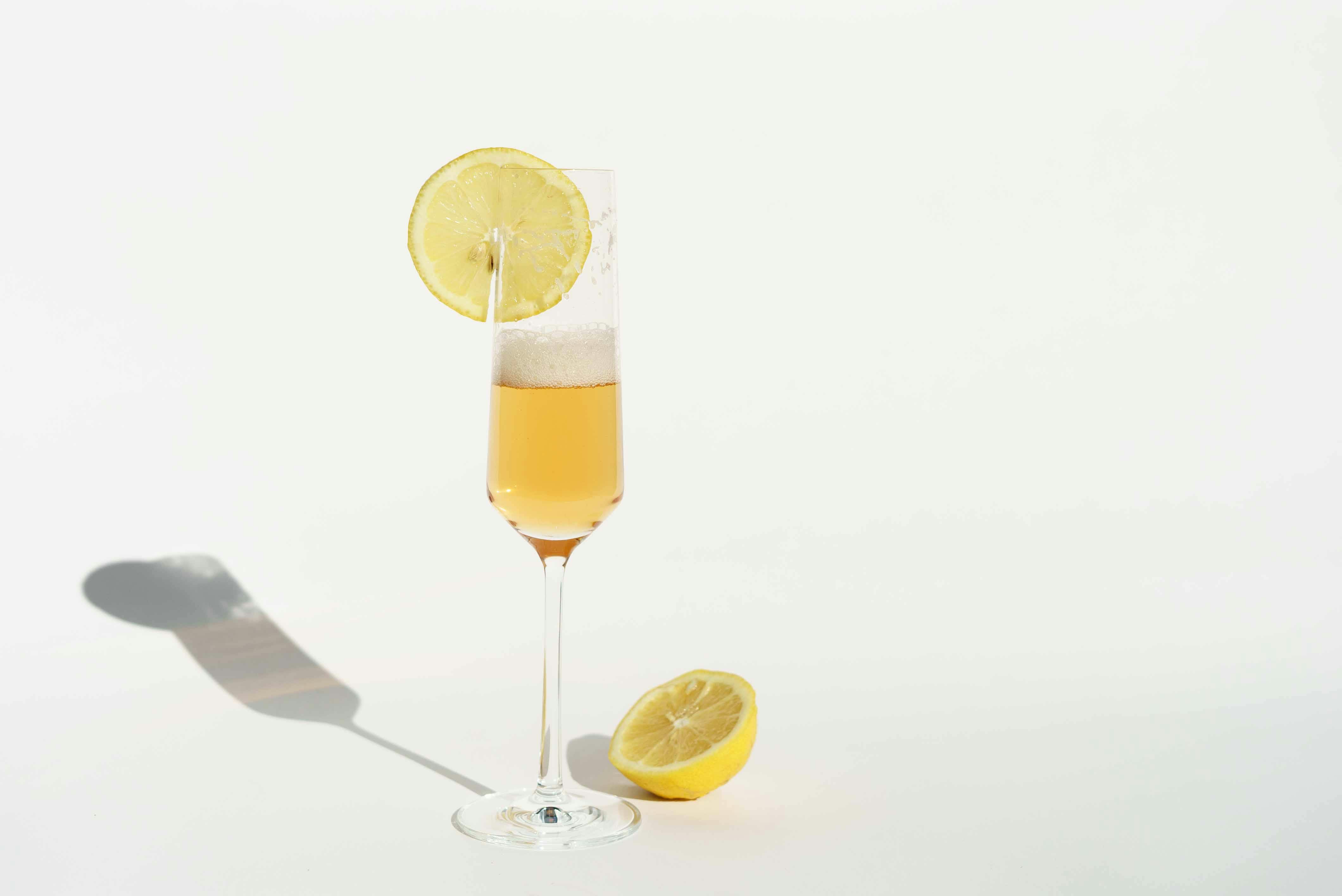 A close-up shot of a fresh cocktail in a champagne glass with lemon garnish, casting a shadow on a white surface.