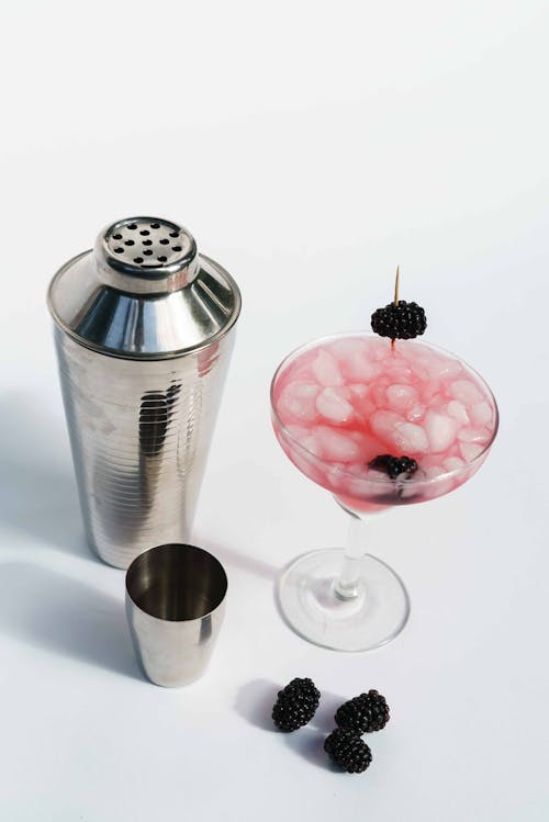 Free High angle of stainless shaker with metal jigger placed near glass of alcohol with blueberries Stock Photo