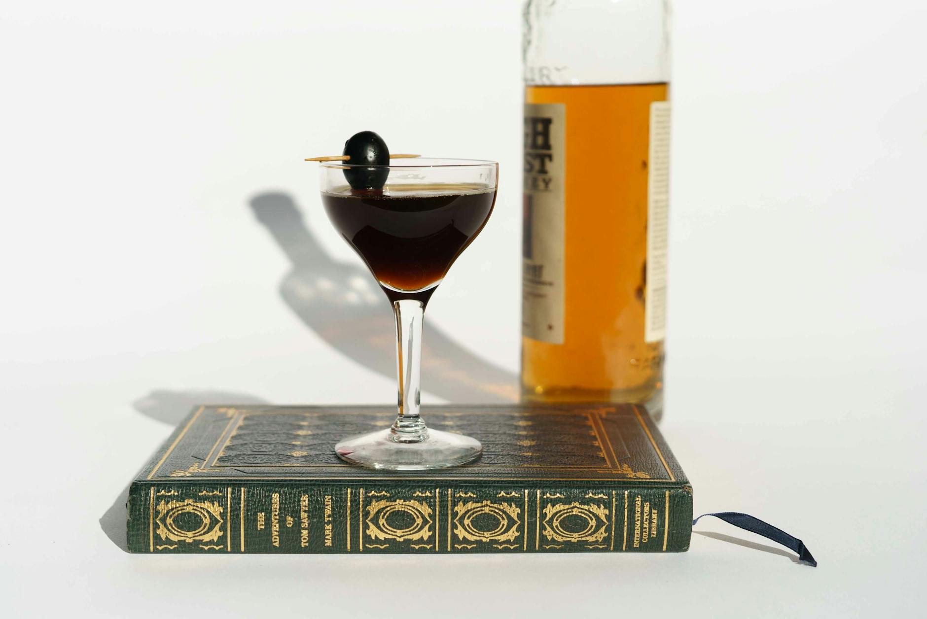 Martini cocktail on book near bottle of whiskey