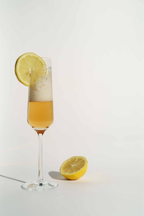 Transparent glass of champagne with foam served with slice of lemon on white background