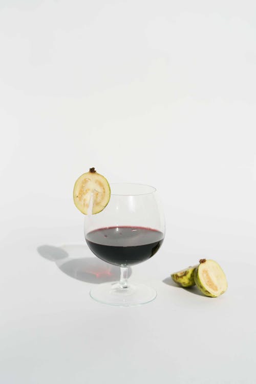 Glass of red wine served with slice of tropical guava on white background