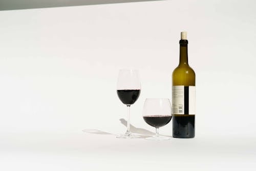 Red wine made from dark colored grape varieties in bottle and glasses placed in white studio
