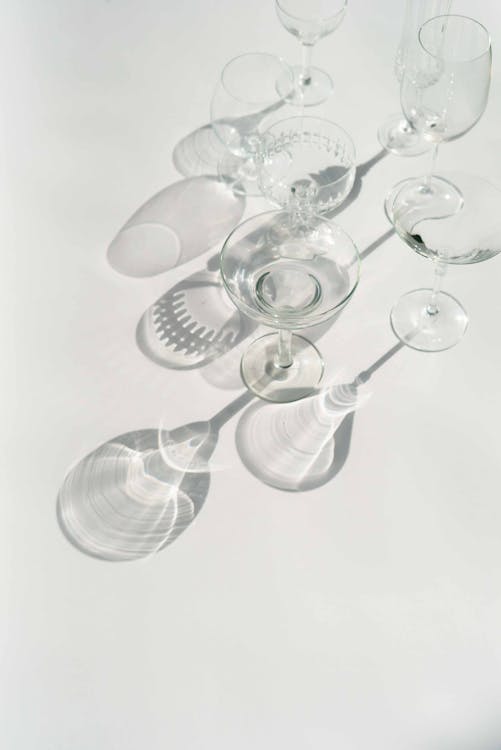 From above of different empty crystal glasses casting shadow on white background in studio