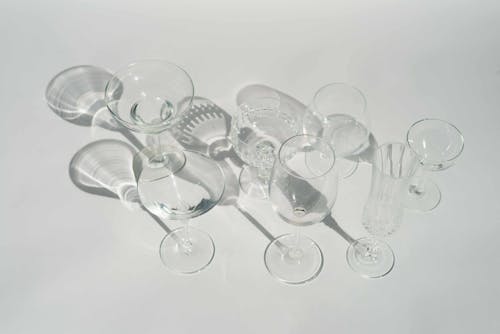 High angle of transparent different glasses for various cocktails and beverages in white studio