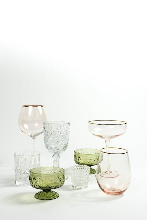 Set of empty various transparent glassware for drinks with different colors and shapes placed in light studio on white background