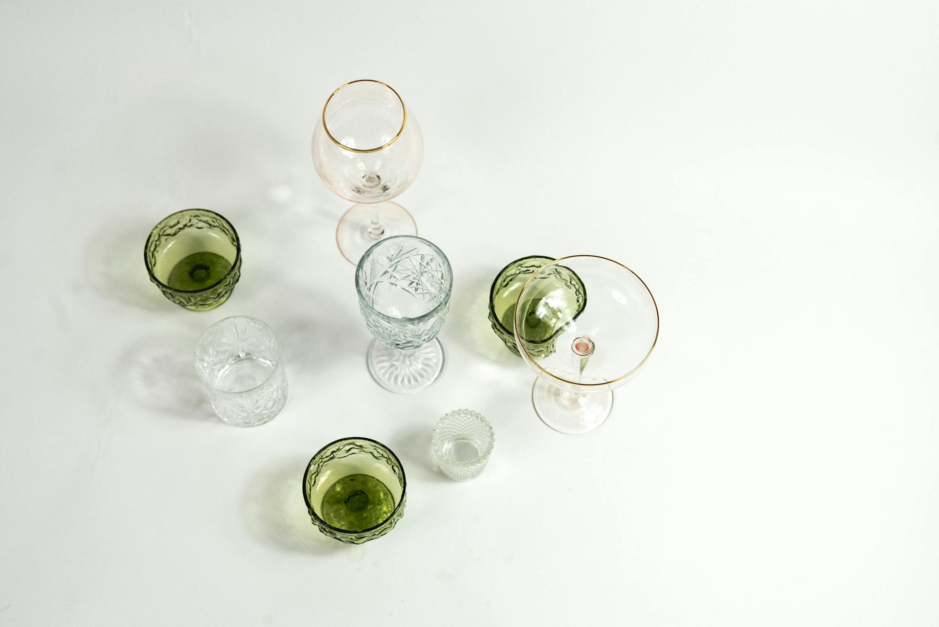 Van bovenaf collectie van glaswerk met verschillende glazen met verschillende kleuren en maten geplaatst op een witte achtergrond in een lichtstudio