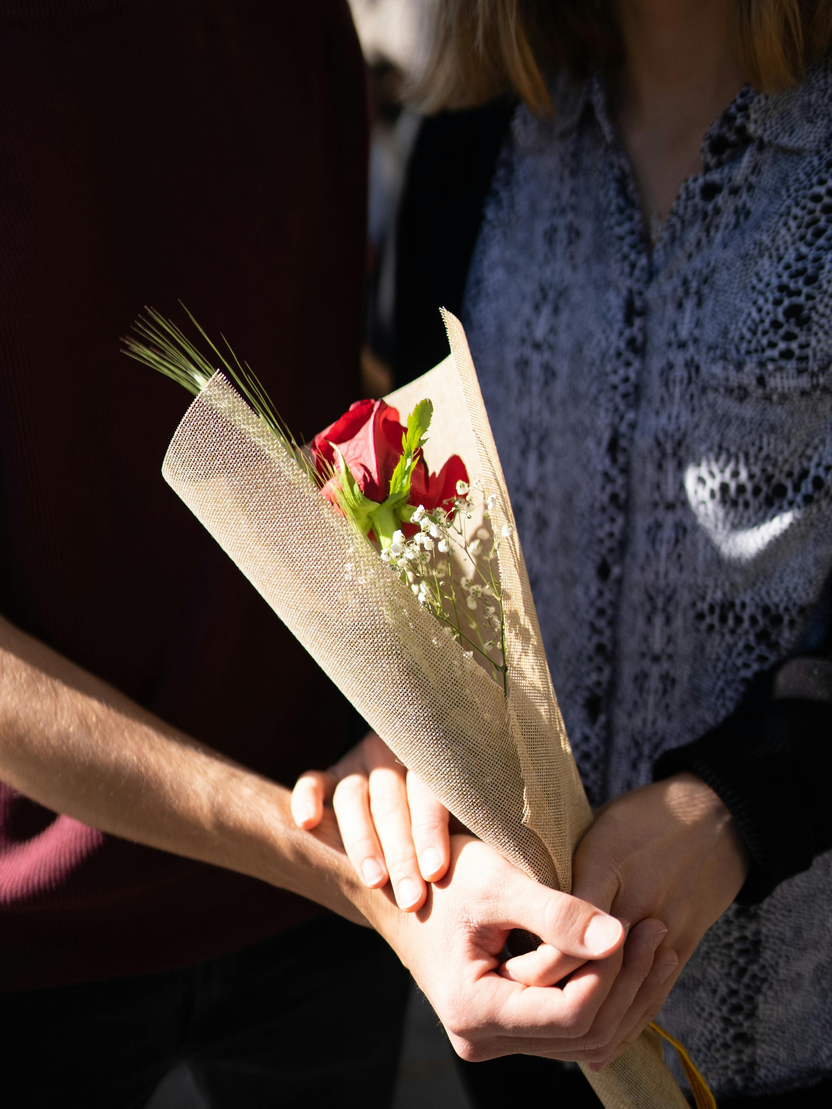 A couple shares a tender moment holding a red rose bouquet in natural light.