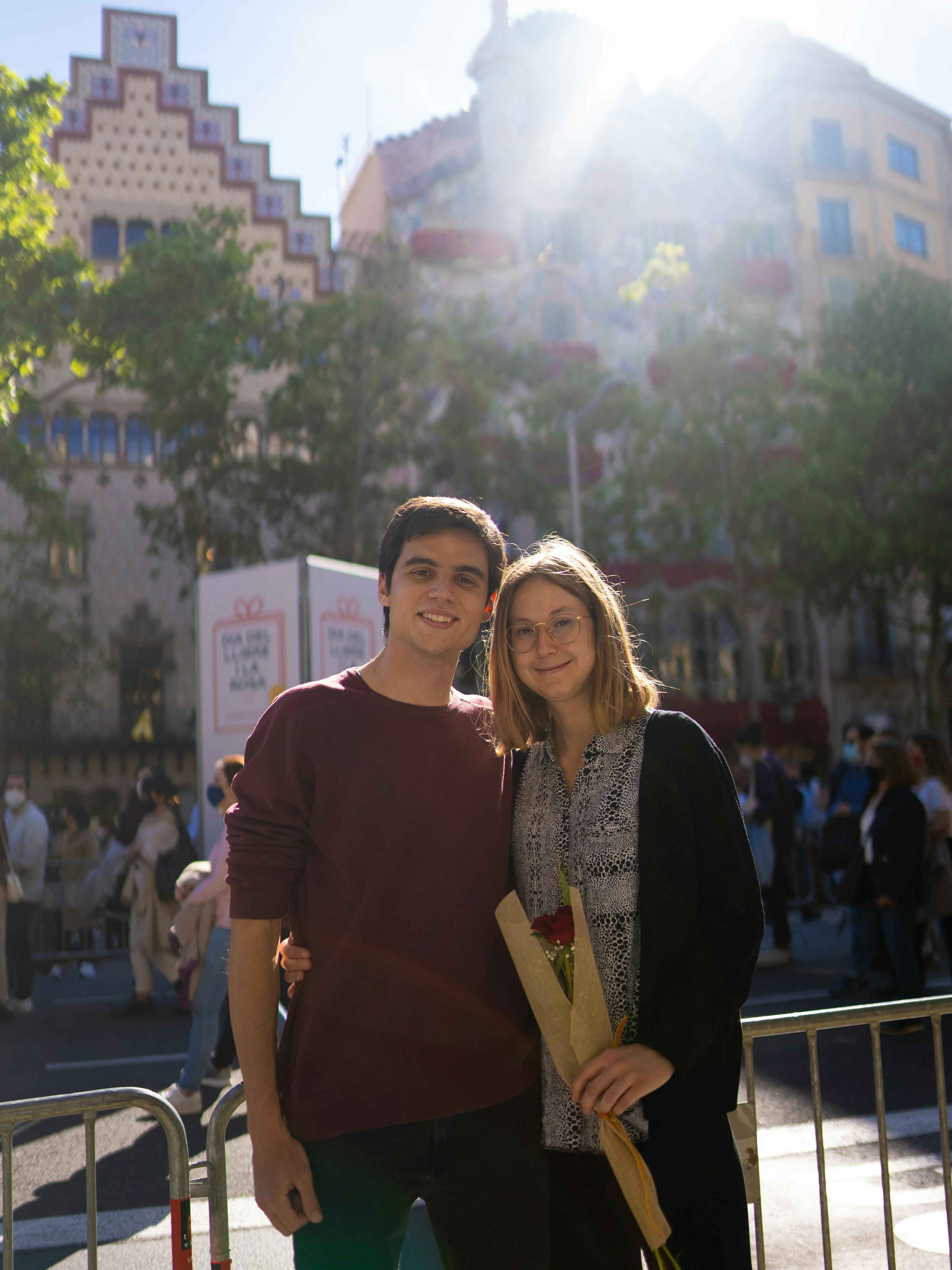 Smiling couple holding a rose during an outdoor festival celebration in sunny weather.