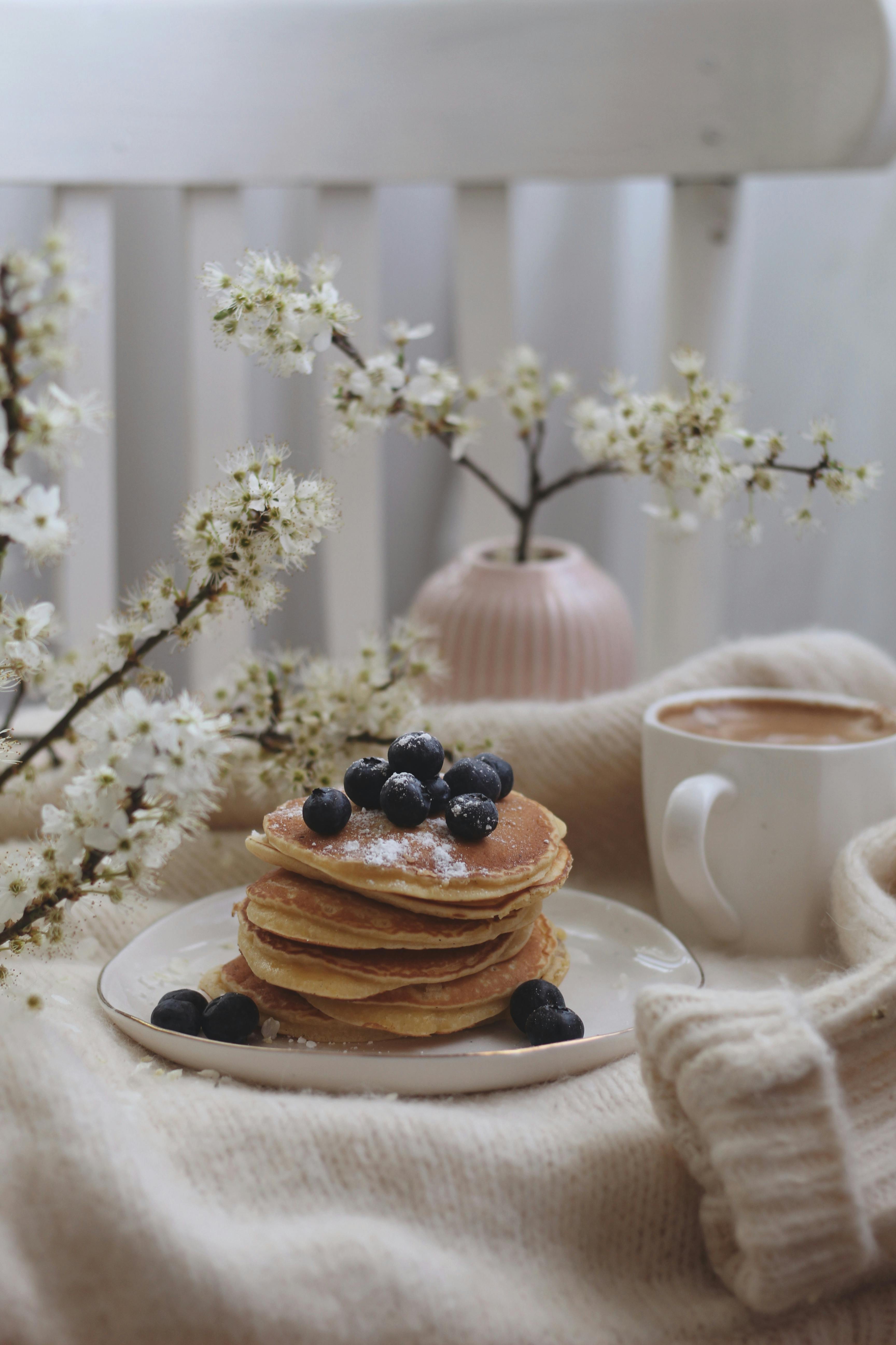 Stack of pancakes with blueberries and coffee in a cozy setting.