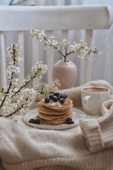 Inviting breakfast setup with blueberry pancakes, coffee, and flowers on a cozy day.