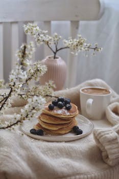 A stack of blueberry pancakes with a warm cup of coffee, surrounded by spring blossoms.