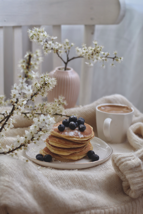 Free A stack of blueberry pancakes with a warm cup of coffee, surrounded by spring blossoms. Stock Photo
